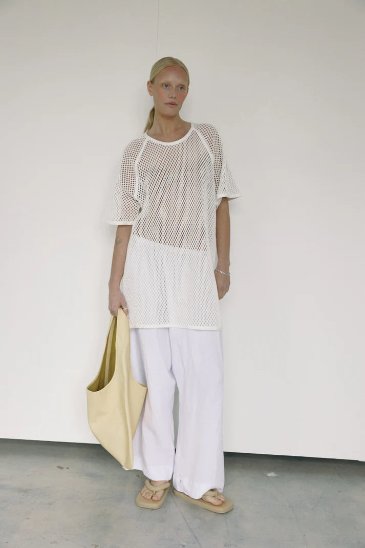 Woman wearing a white mesh top and white pants holding a light yellow bag against a plain background Vancouver Paloma Leather Bag Canada