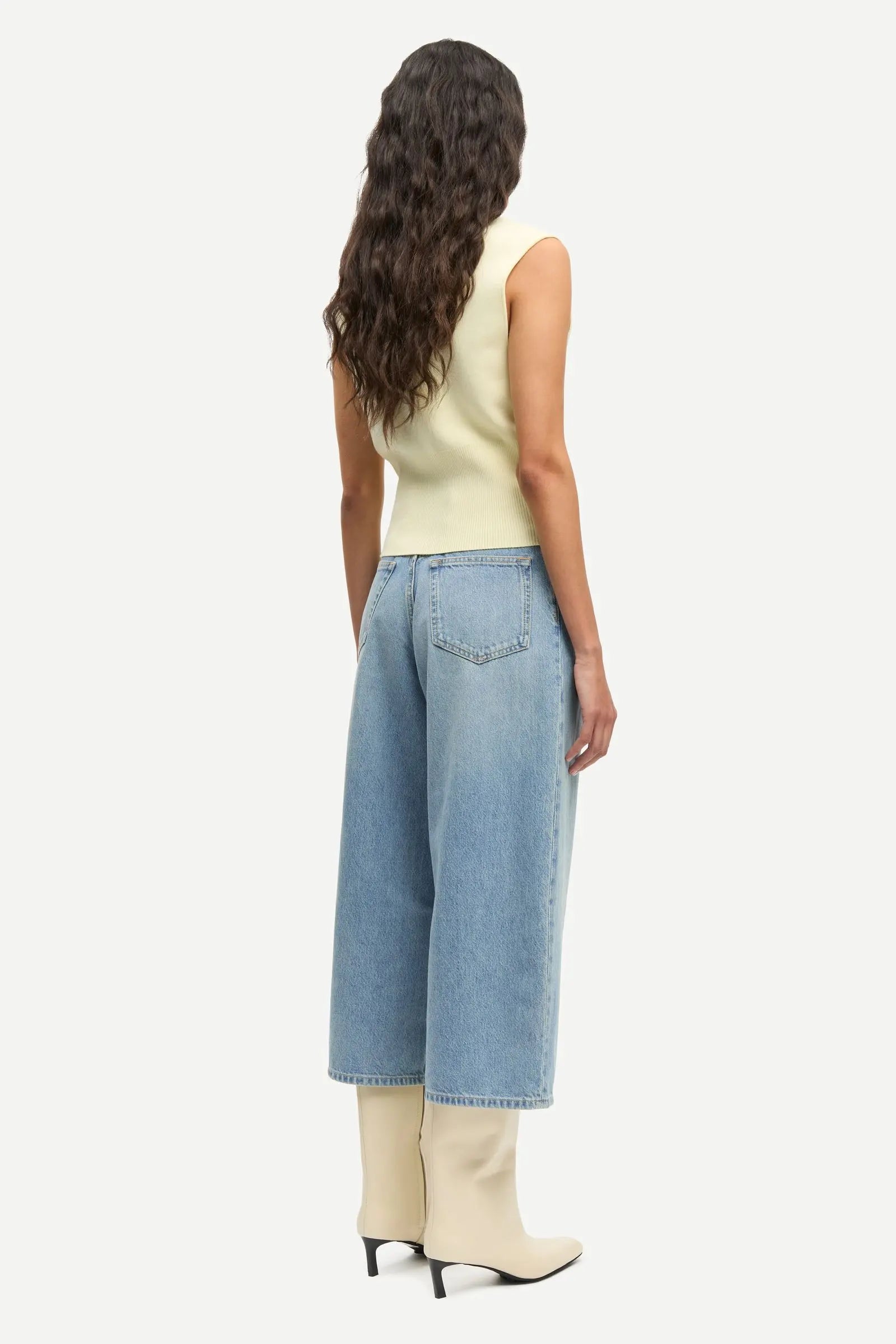 Woman wearing a light yellow sleeveless top and blue jeans on a white background samsoe samsoe sale paloma vancouver